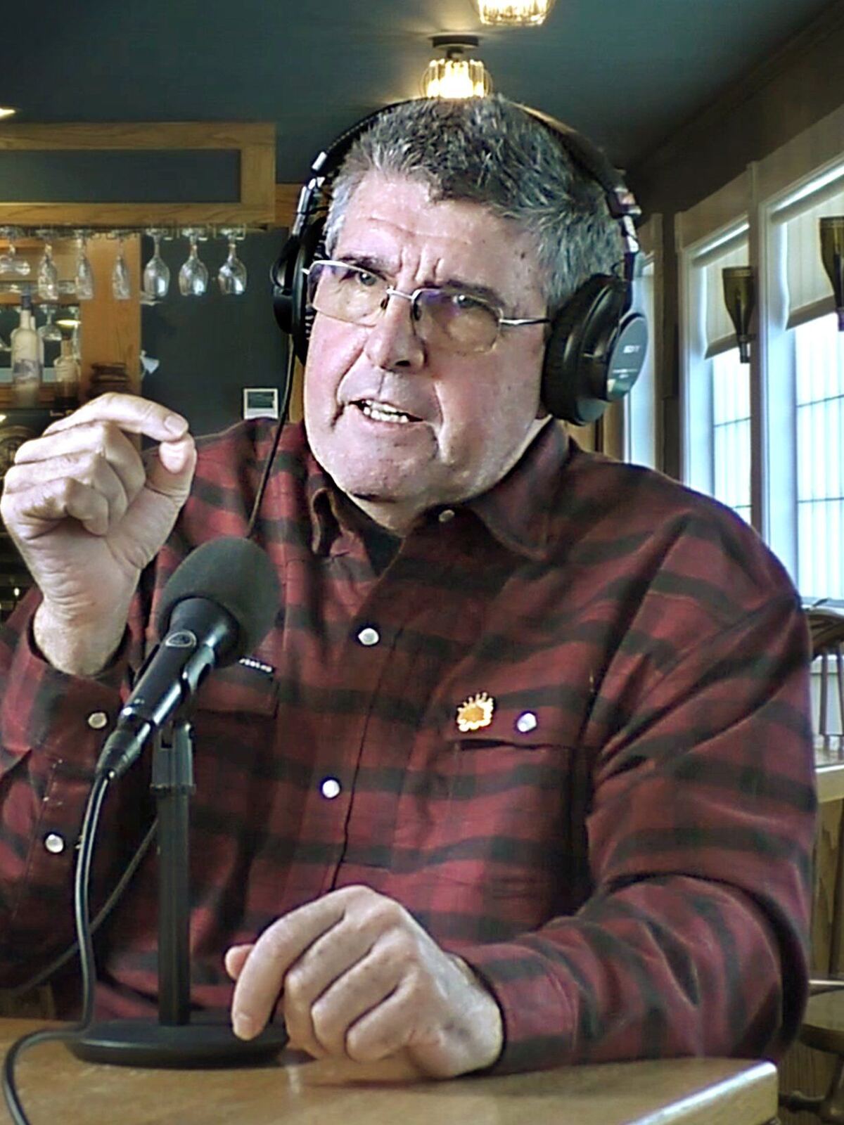 Dennis Pratt, in a red plaid shirt, speaking at a microphone.