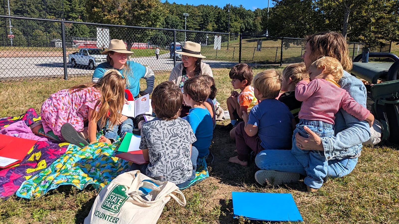 Parents and children gathered on blankets in a sunny field, reading together.