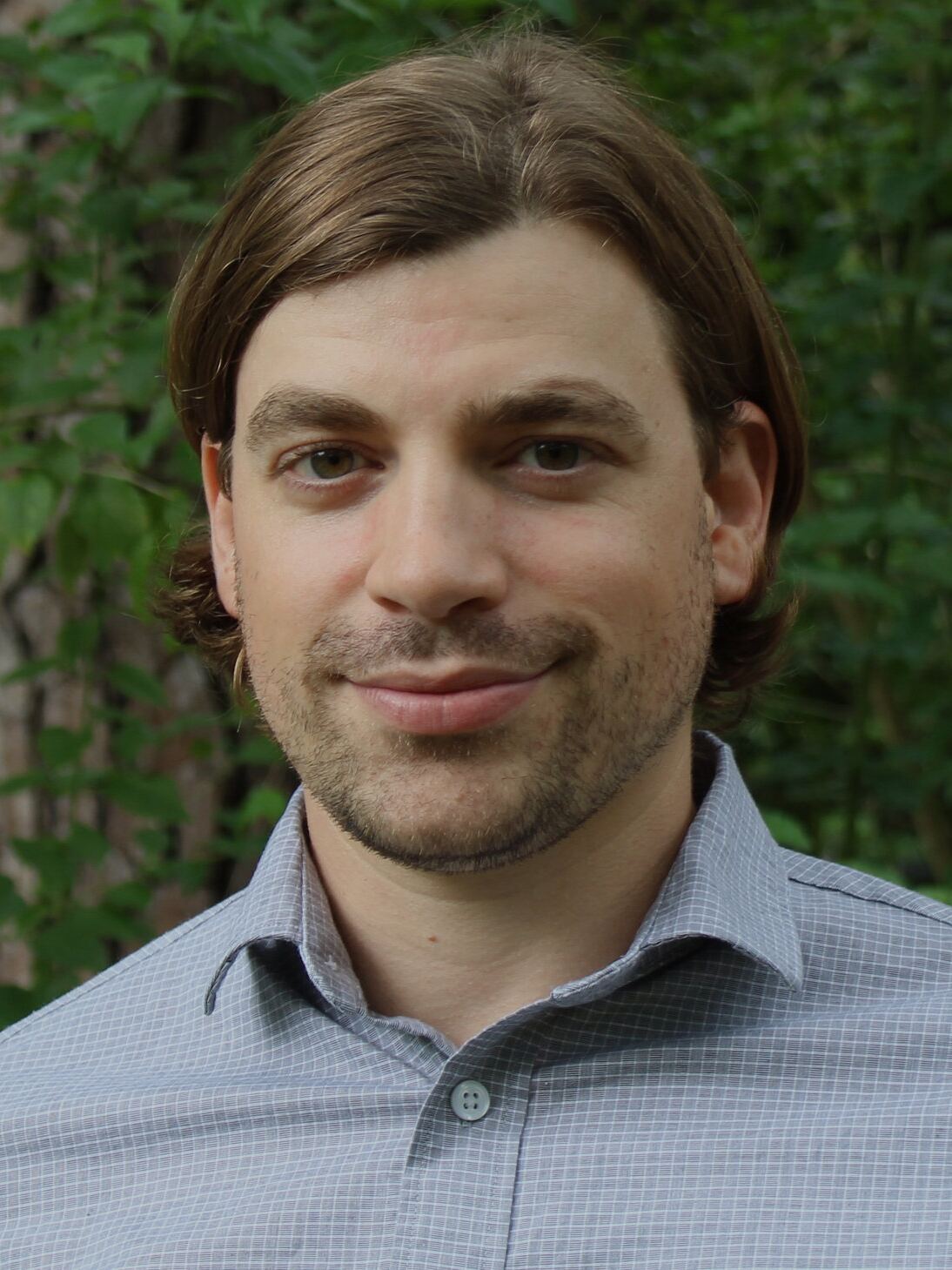 Joe Norman, in a gray shirt, in front of green foliage.
